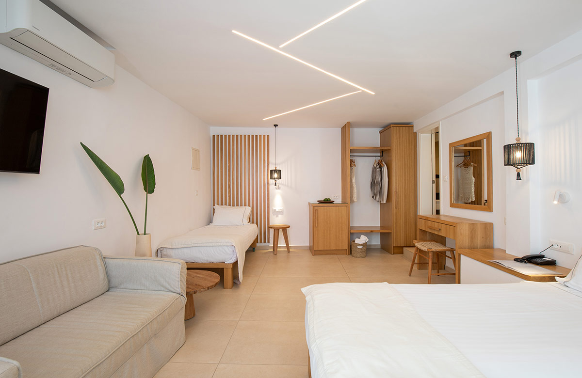 Spacious Triple Standard Room interior at Damianos Hotel in Mykonos Town with sofa bed, single bed, wooden furniture and modern lighting