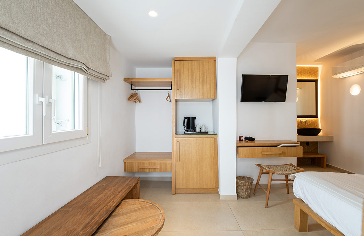 Hotel room in Mykonos Town at Damianos Hotel featuring minimalist wooden furnishings, open closet space and modern vanity area