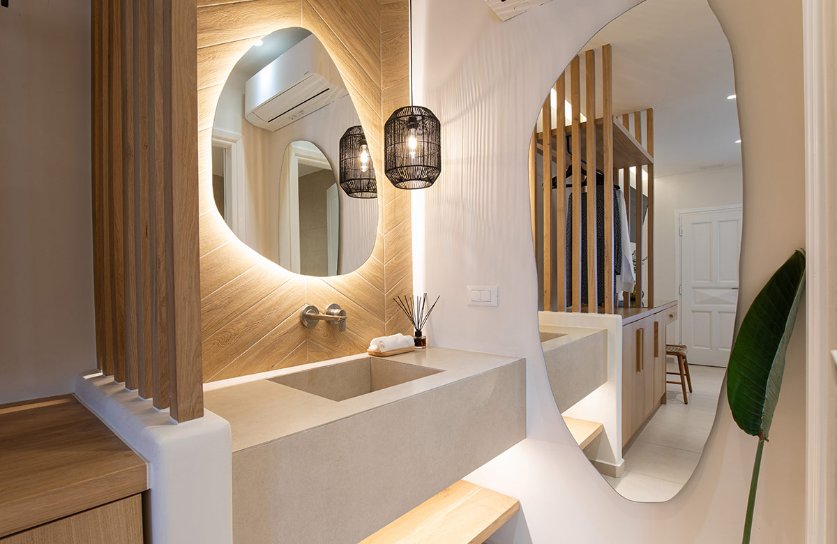 Modern bathroom vanity in hotel room in Mykonos Town at Damianos Hotel with illuminated round mirror and natural wood accents