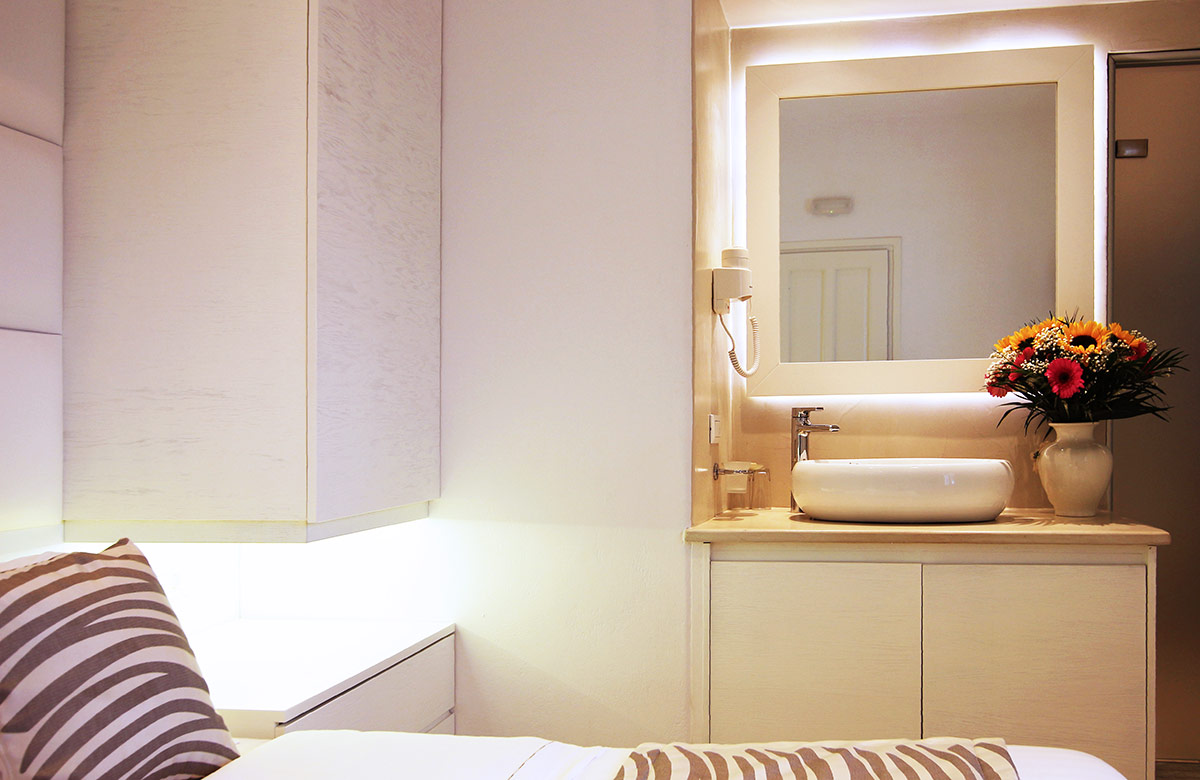 Hotel room in Mykonos Town at Damianos Hotel featuring illuminated vanity mirror, elegant sink and soft ambient lighting
