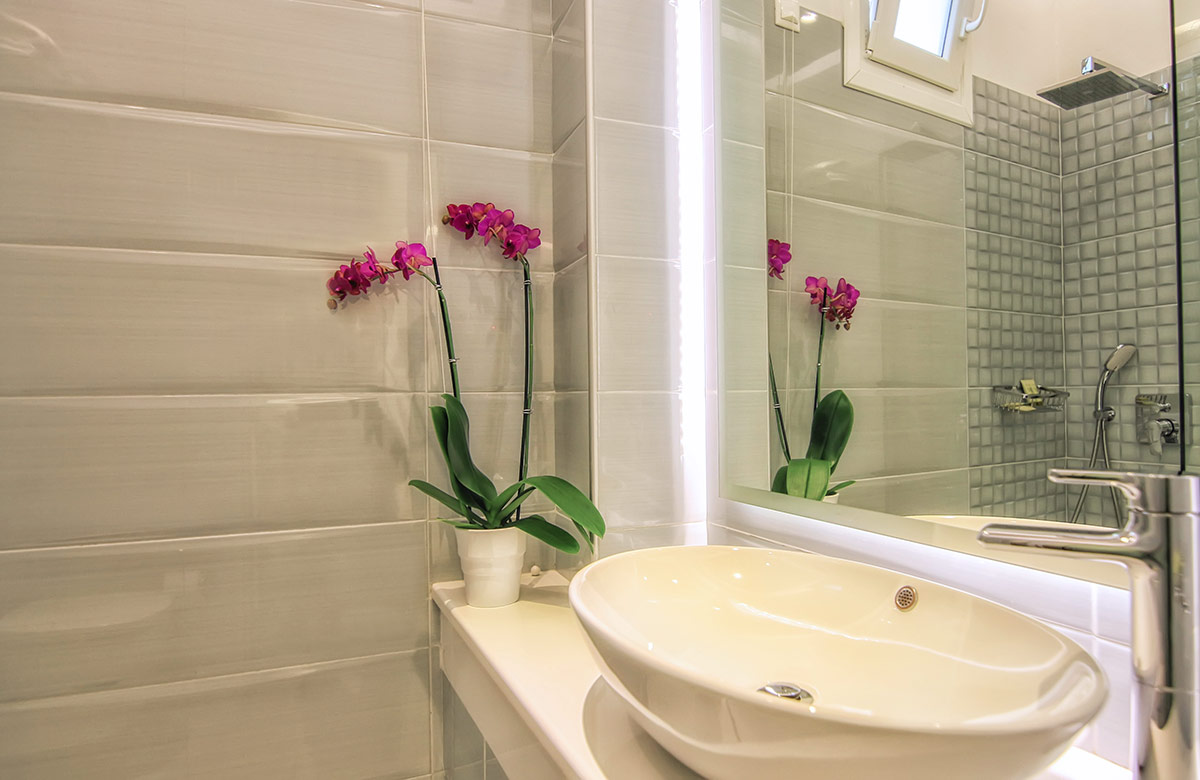 Modern bathroom in hotel room in Mykonos Town at Damianos Hotel with oval sink, illuminated mirror and walk-in shower